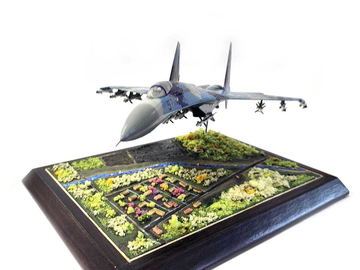 Handcrafted fighter aircraft scale model displayed over a miniature landscape
